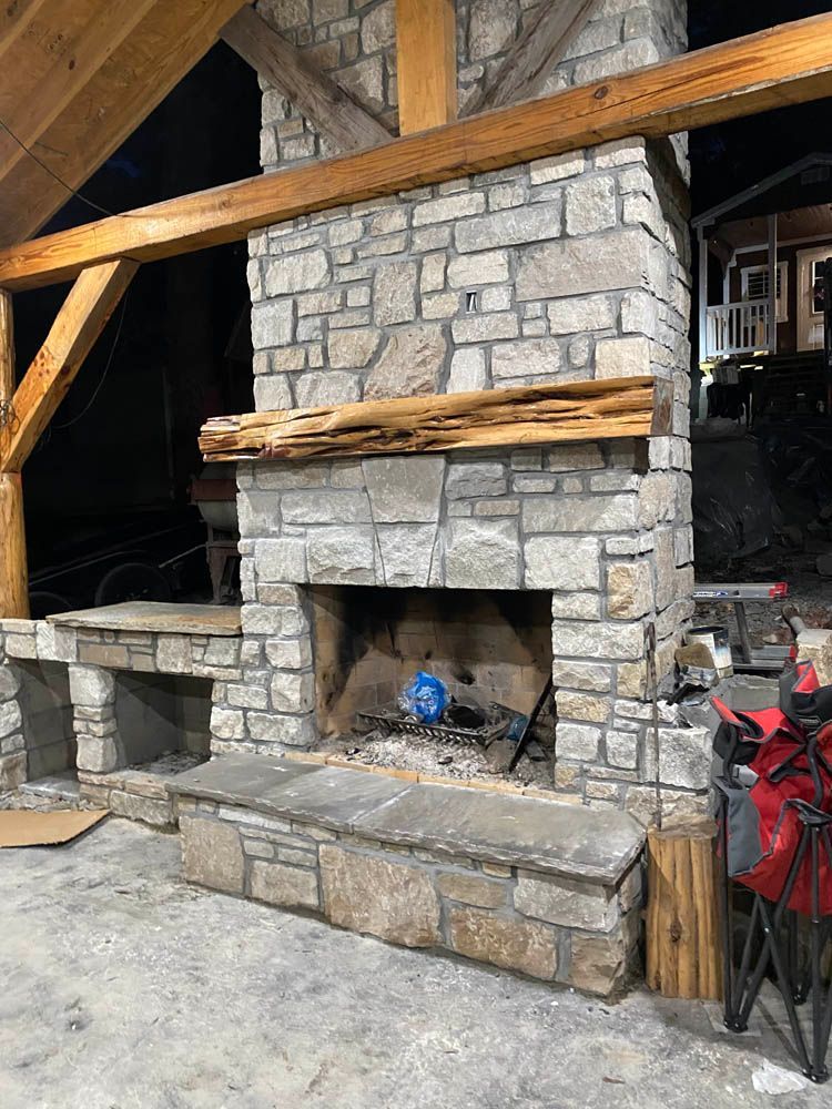 A stone fireplace with a wooden mantle is sitting under a wooden roof.