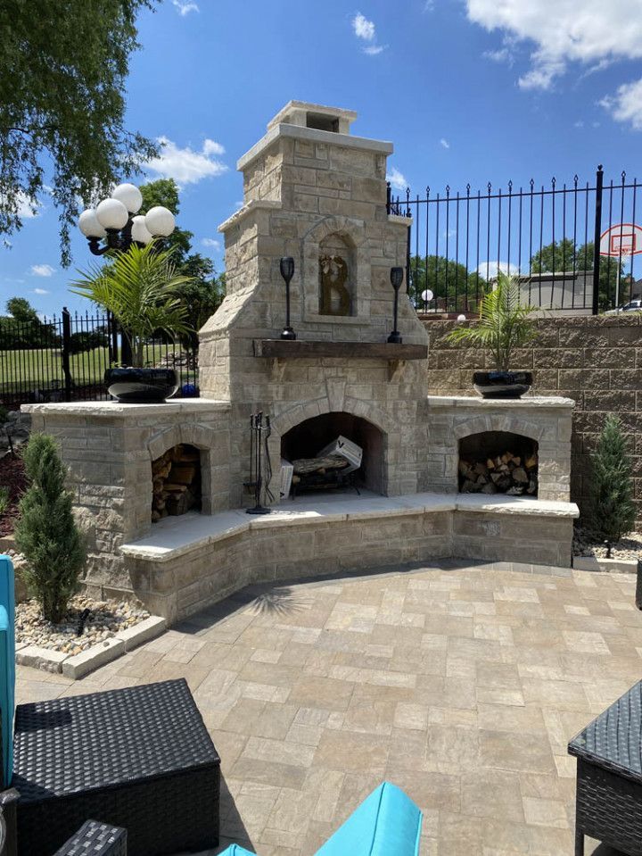 A large stone fireplace is sitting on a patio next to a fence.