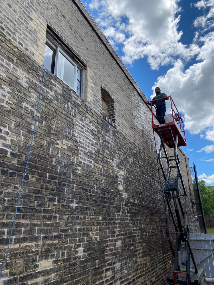 A man is standing on a ladder cleaning a brick wall.