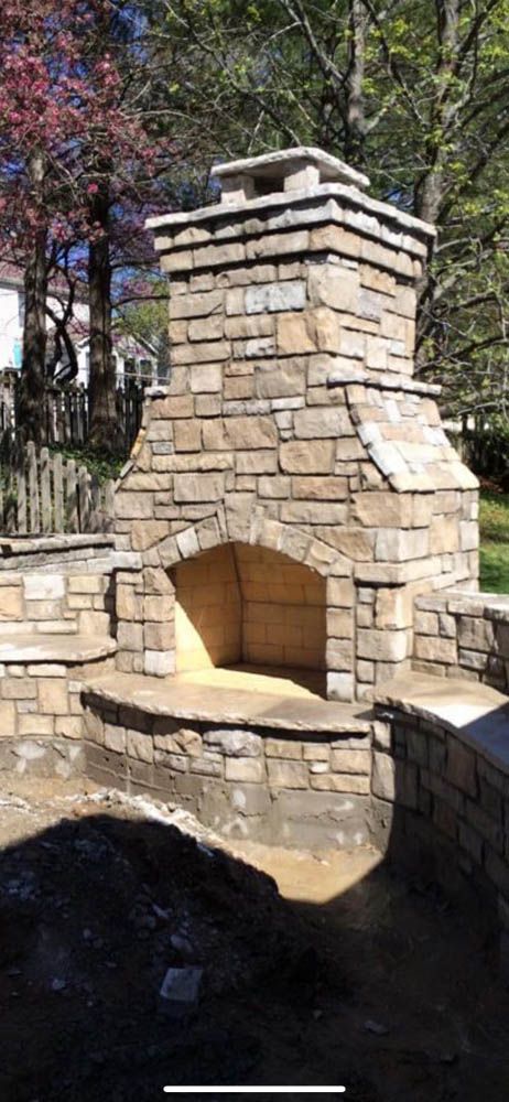 A stone fireplace in a backyard with trees in the background.