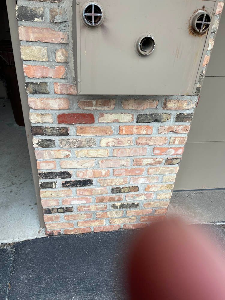 A person is pointing at a brick wall with two holes in it.