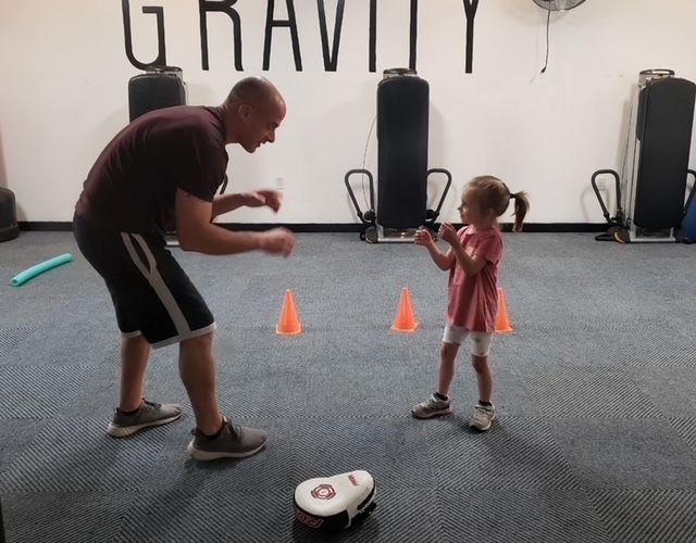 A man and a little girl are playing in a gym with the word gravity on the wall