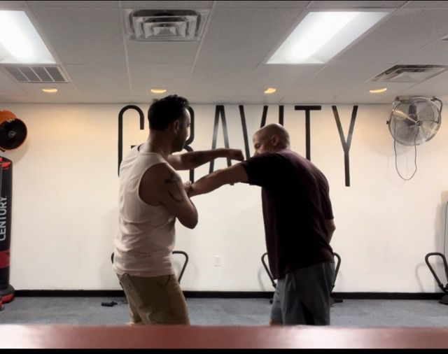 Two men are fighting in a gym with the word gravity on the wall