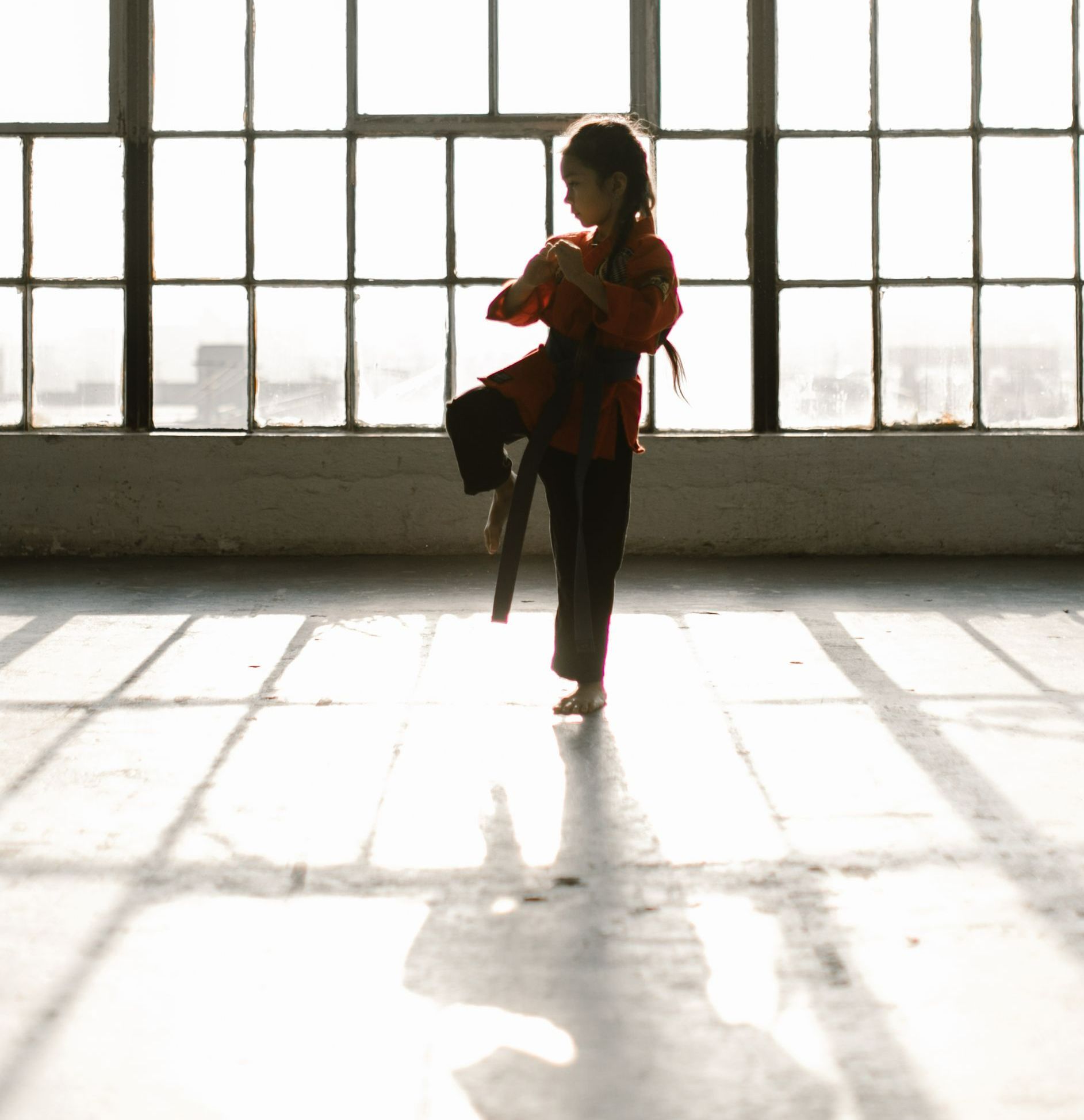 A girl is practicing karate in front of a window