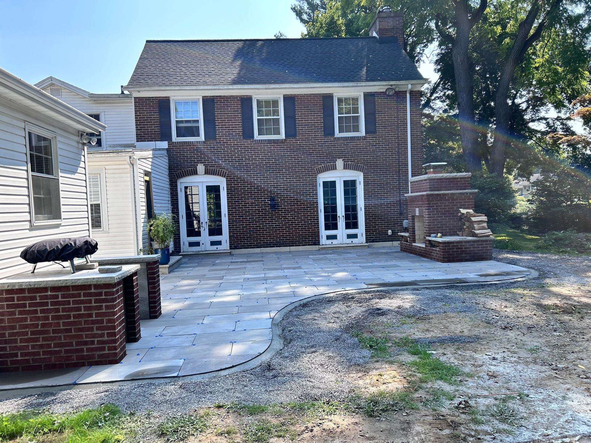 A brick house features a newly installed stone patio, an outdoor brick fireplace, and a partial brick kitchen island.