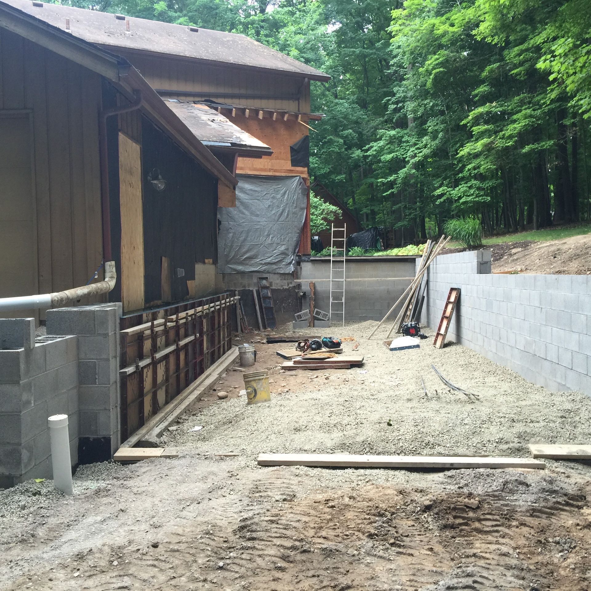A residential construction site with a concrete block retaining wall, scaffolding, and wood forms beside a house.