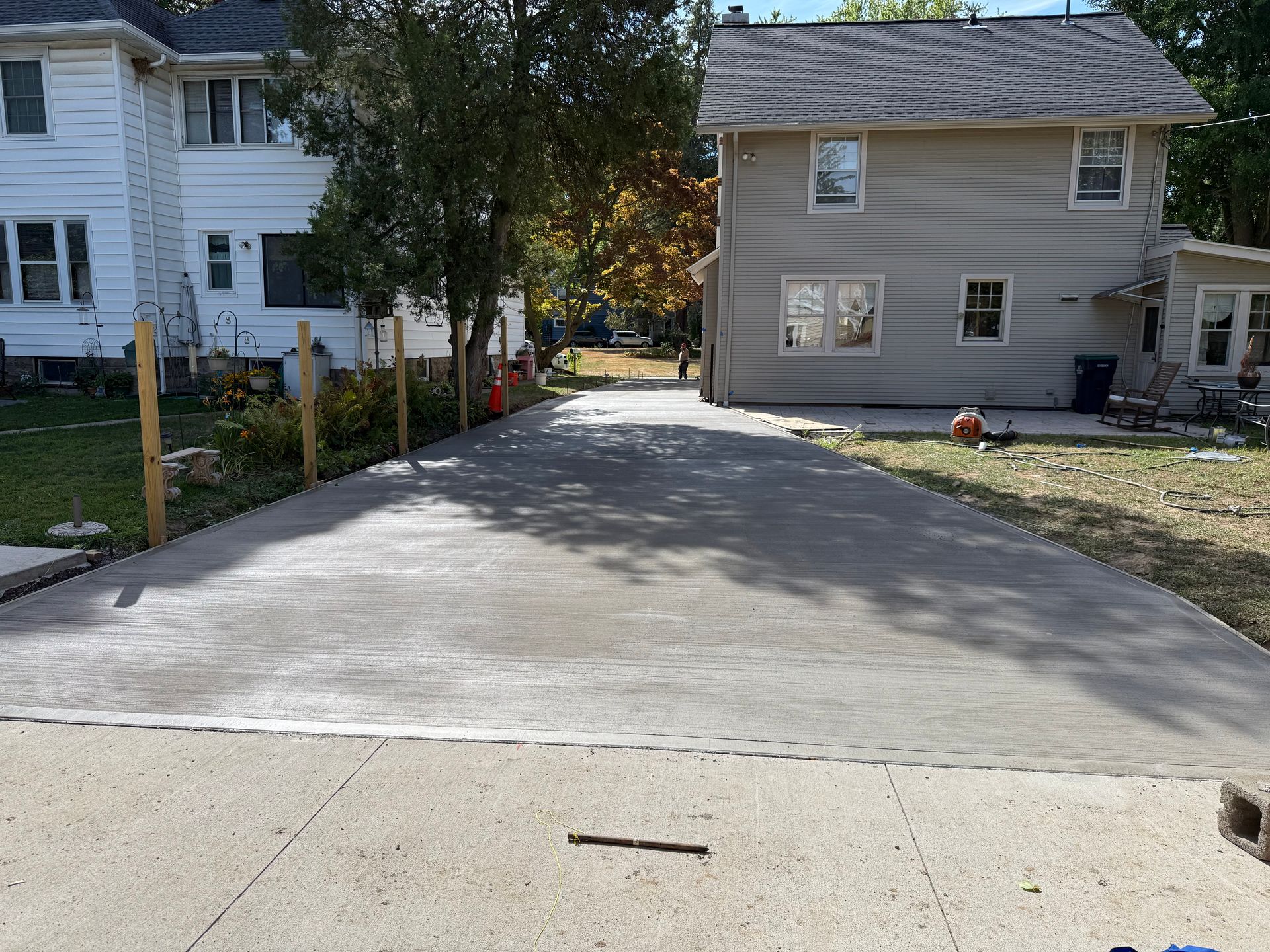 A newly poured concrete driveway leads between two houses, with wooden fence posts lining the left side.