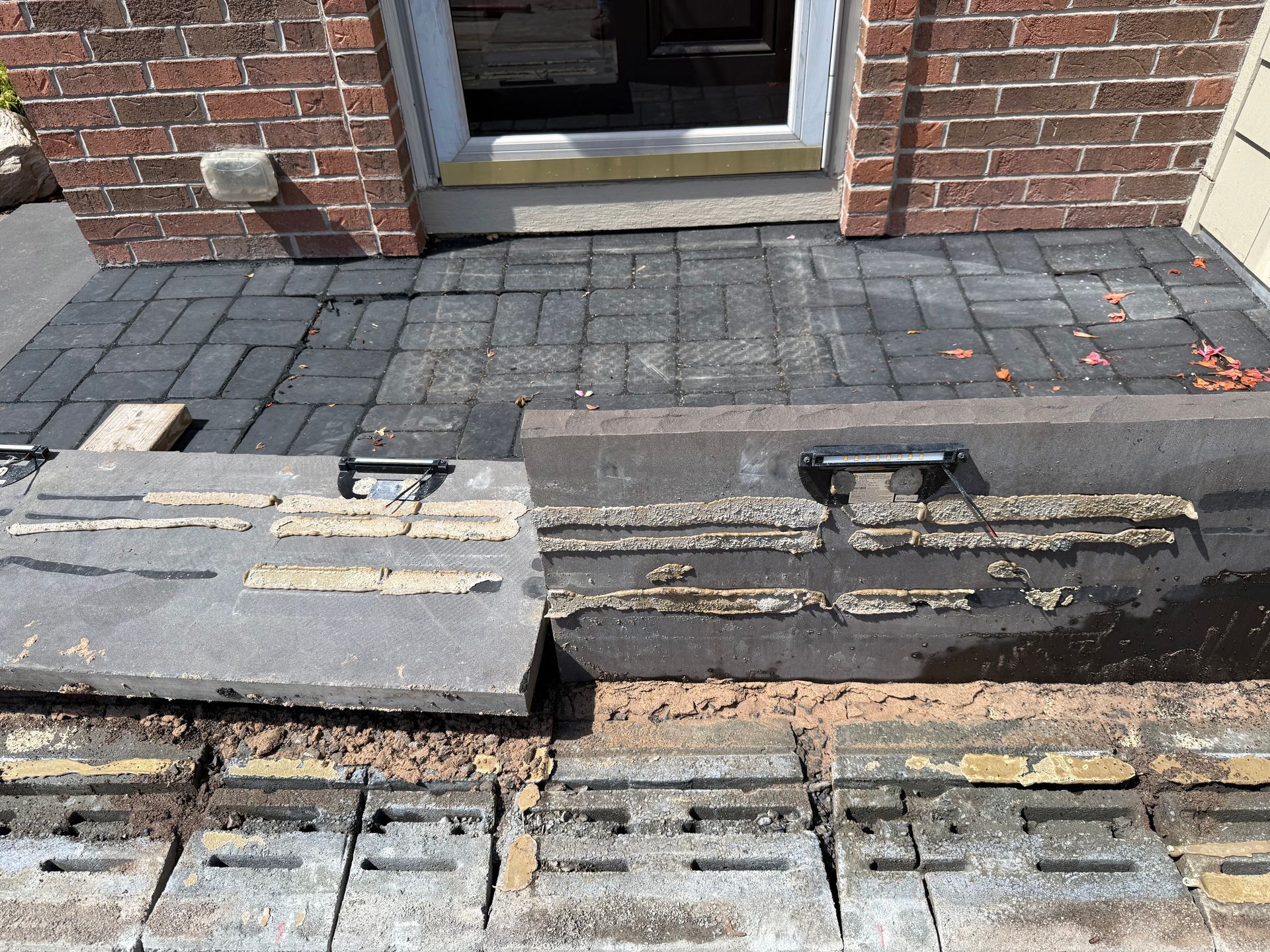 A detached concrete slab with adhesive residue resting in front of a brick building entrance with gray paver steps.