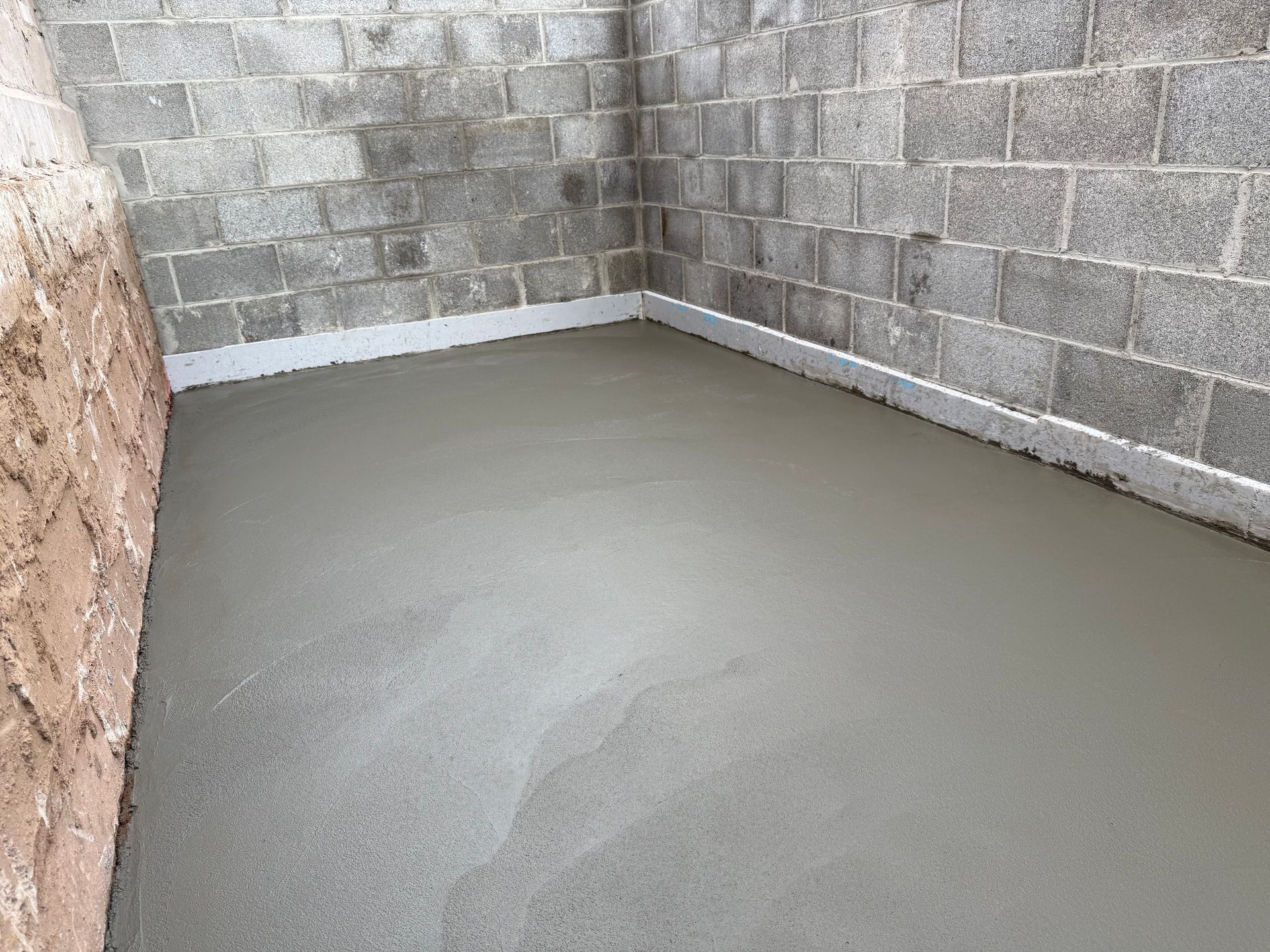 A freshly poured, smooth gray concrete floor inside a room with cinder block walls.