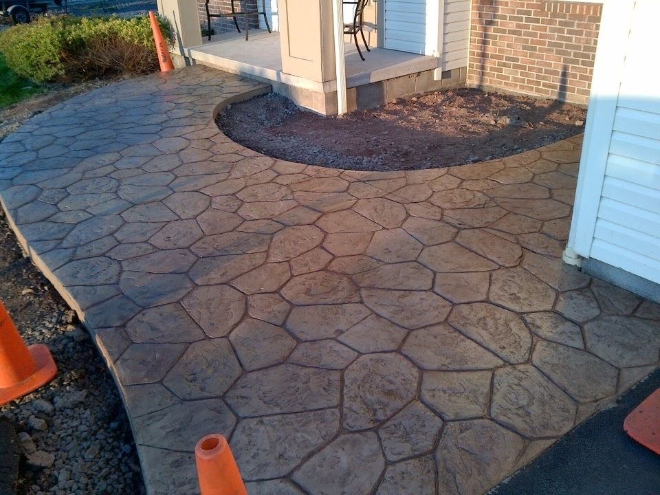 Stamped concrete walkway with a stone pattern in brown tones leading to a residential porch, flanked by orange cones.