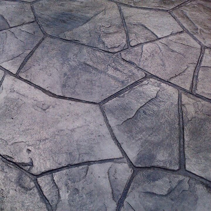 A close-up of grey stamped concrete designed to resemble irregular natural stone pavers with dark, recessed grout lines.