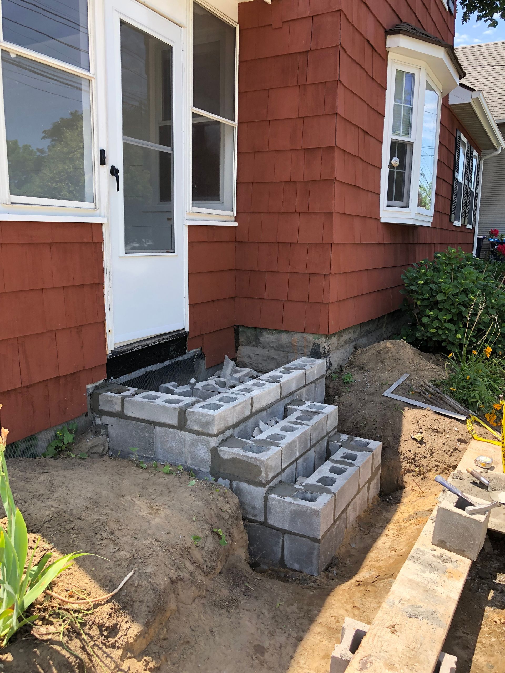 A red-sided house features a set of unfinished concrete block steps currently under construction leading to a white door.