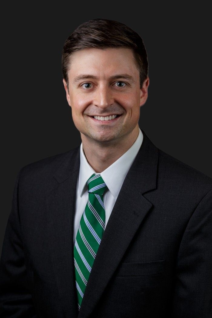 Graham Thompson Portrait of a smiling man in a dark suit and green striped tie on a dark background