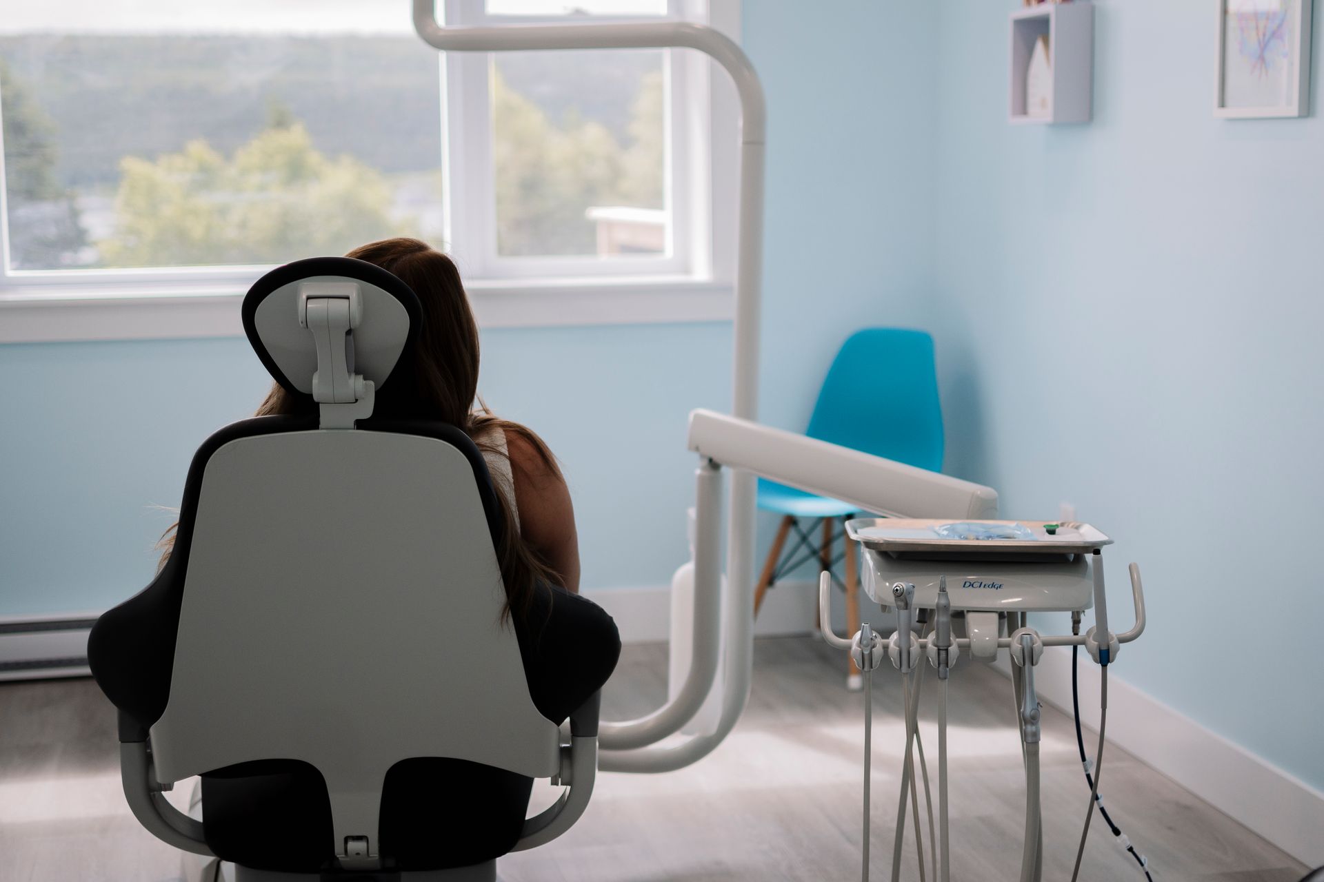 Person seated in a dental chair, facing away from the camera, in a bright blue dental room. Harbour Grace Dental Hygiene
