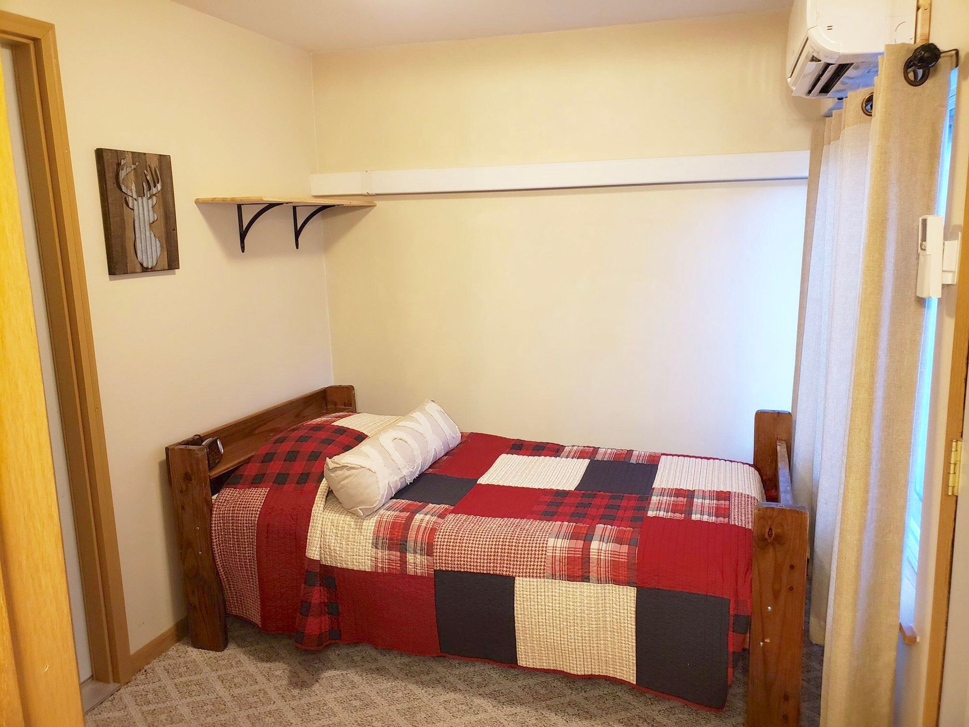 Small bedroom with a wooden bed, red quilt, and a shelf on the wall.