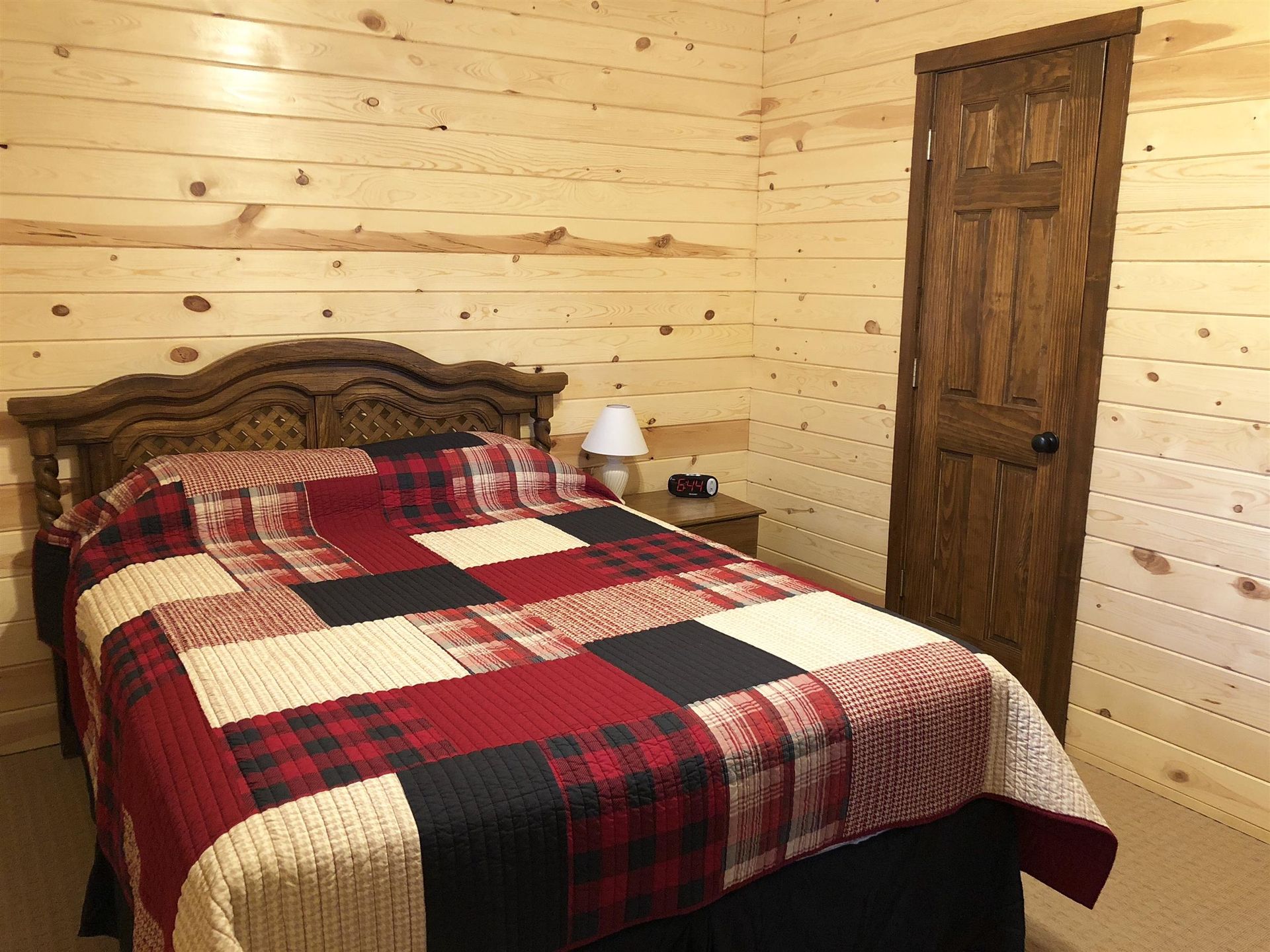 Bedroom with a wooden paneled wall, a bed with a red quilt, and a closed wooden door.