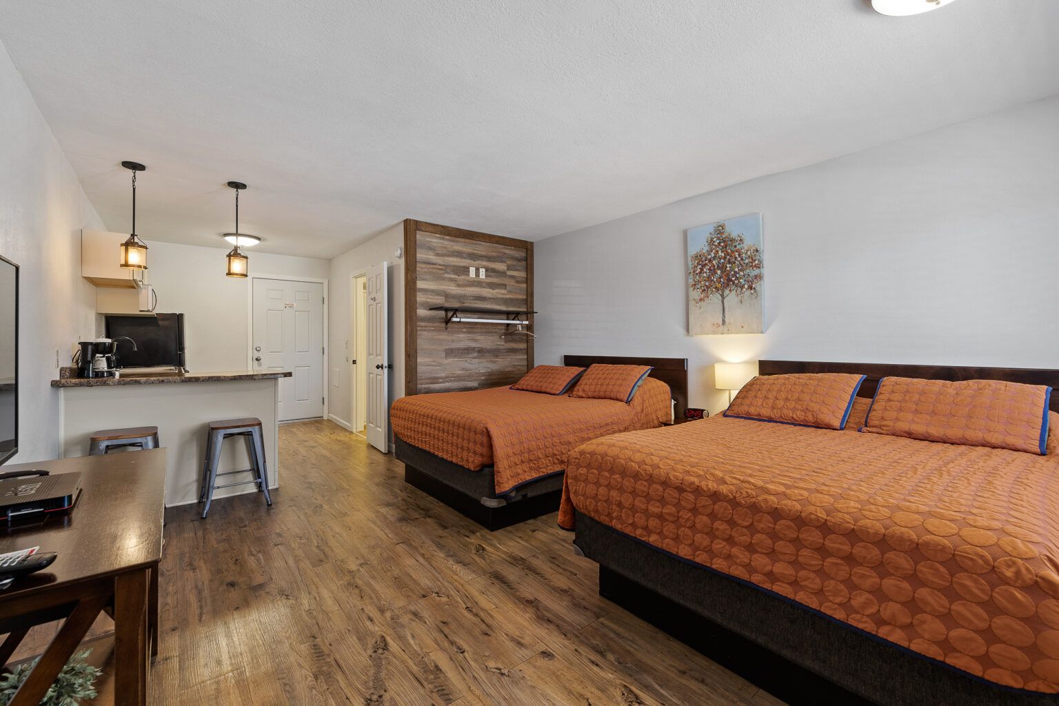 Hotel room with two queen beds, a small kitchen, and a wooden accent wall.