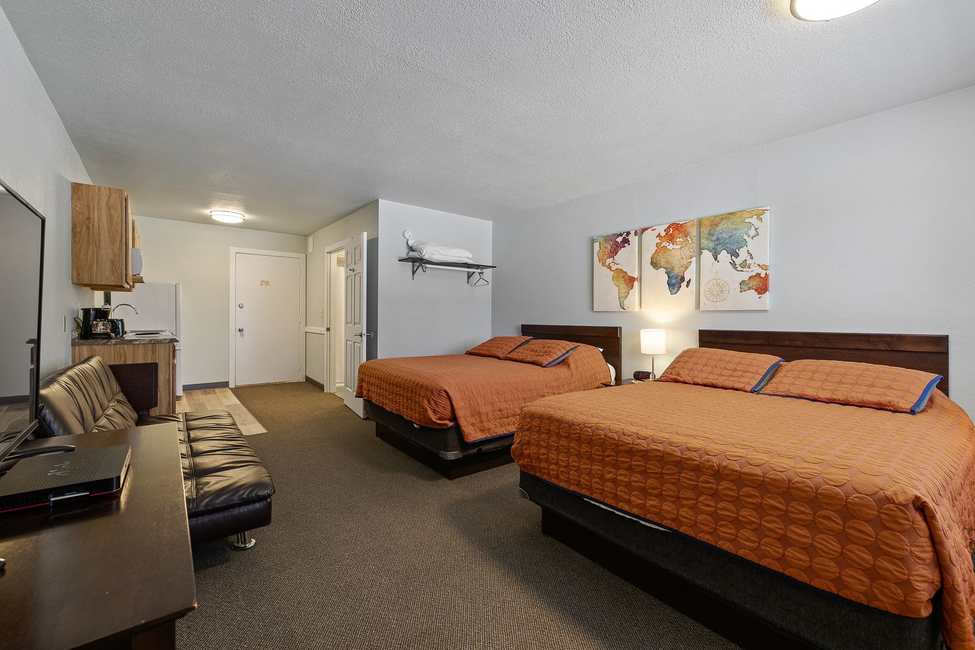 Hotel room with two beds, small kitchenette, and world map artwork on the wall.