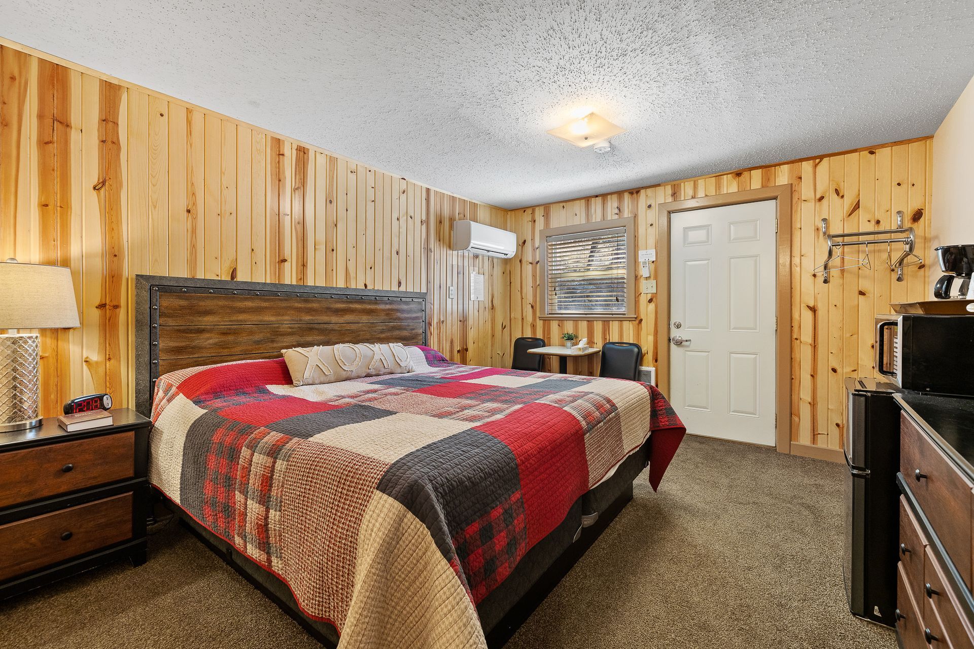 Motel room: wood-paneled walls, bed with quilt, bedside tables, microwave, small table, door, window unit.