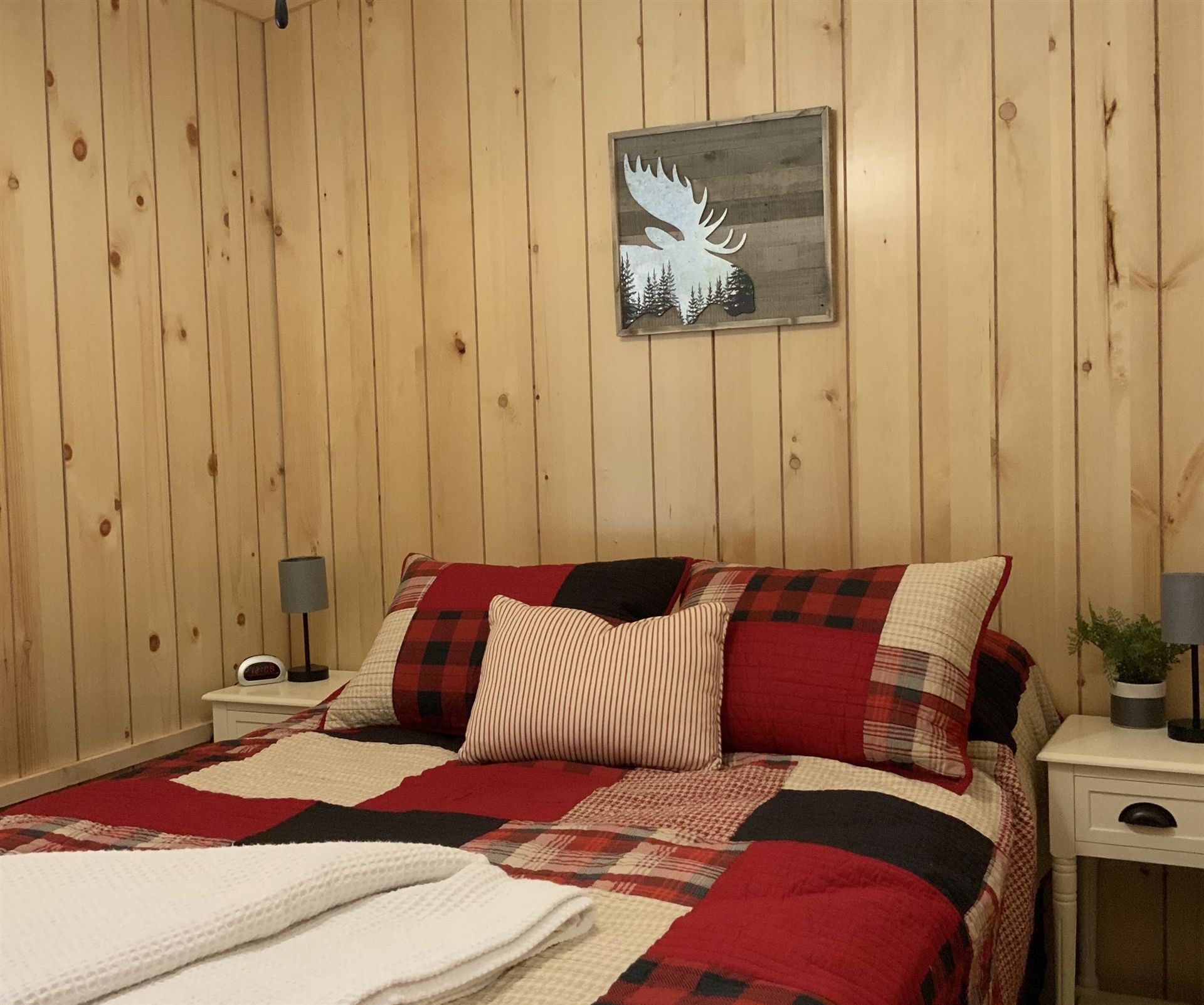 Bedroom with red and black plaid bedding, wood-paneled walls, and a moose art piece.