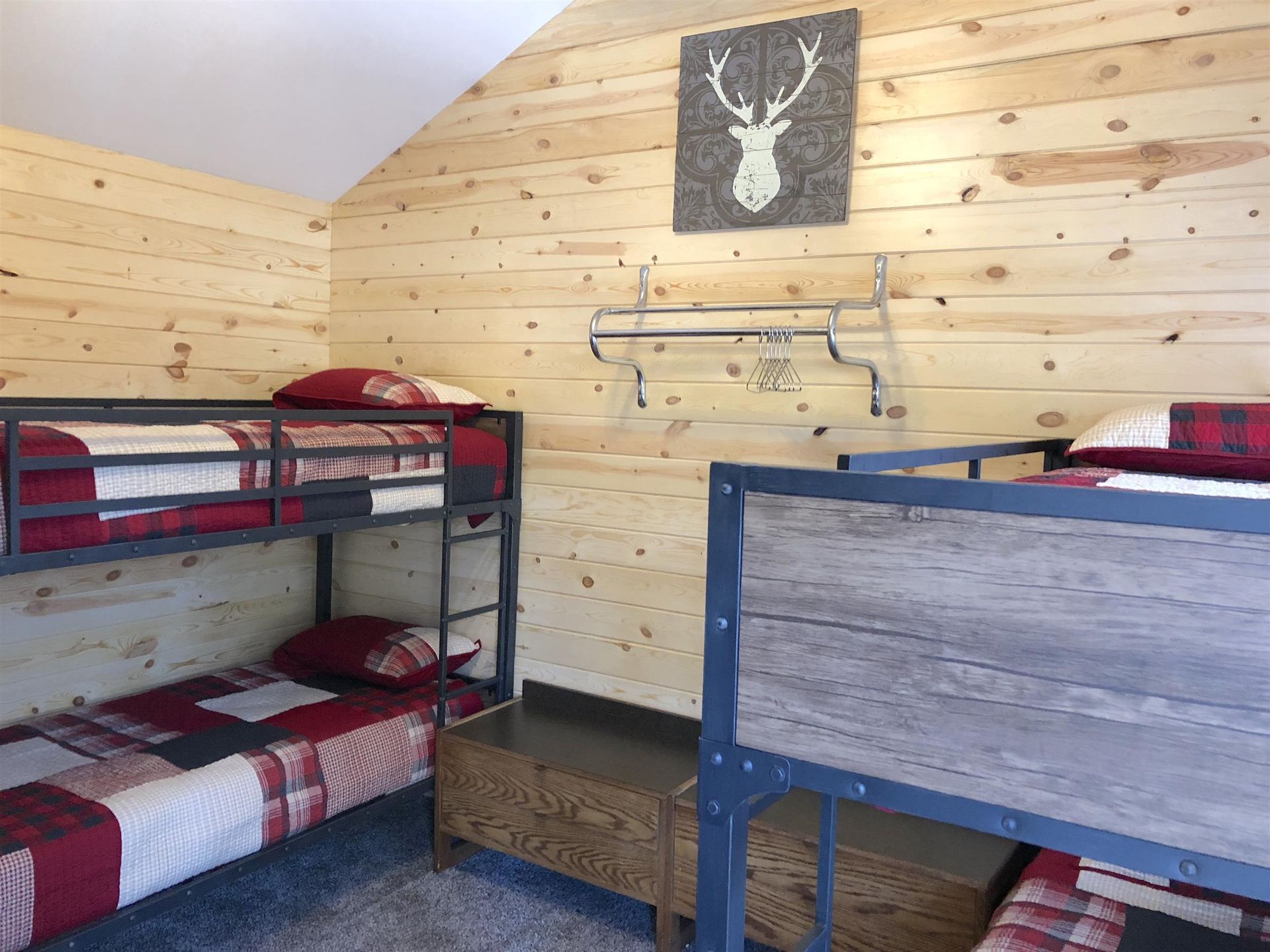 Bunk beds in a cabin-style bedroom, wood-paneled walls, deer head decor, red plaid bedding.
