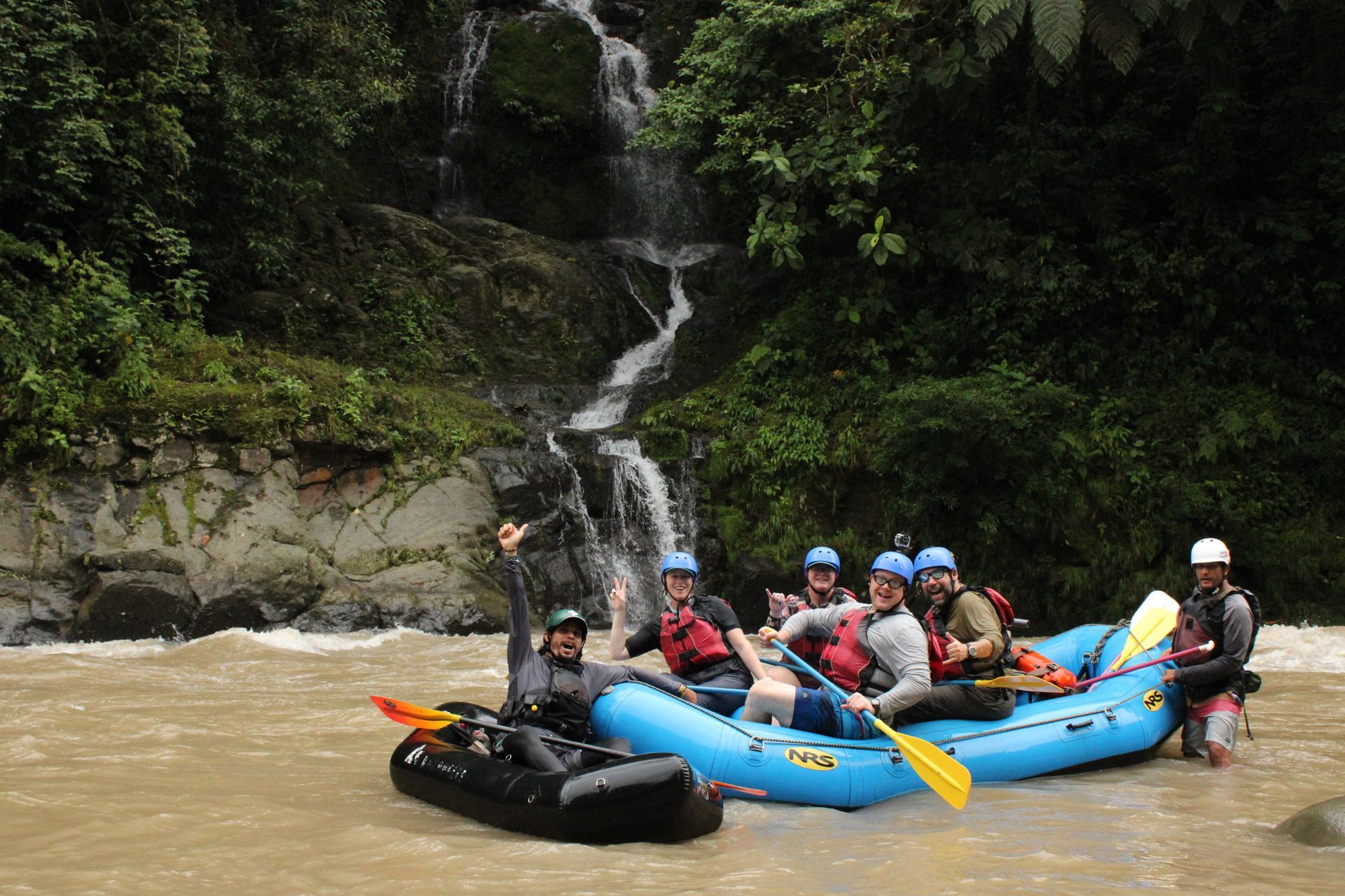 A group of people are rafting down a river near a waterfall.