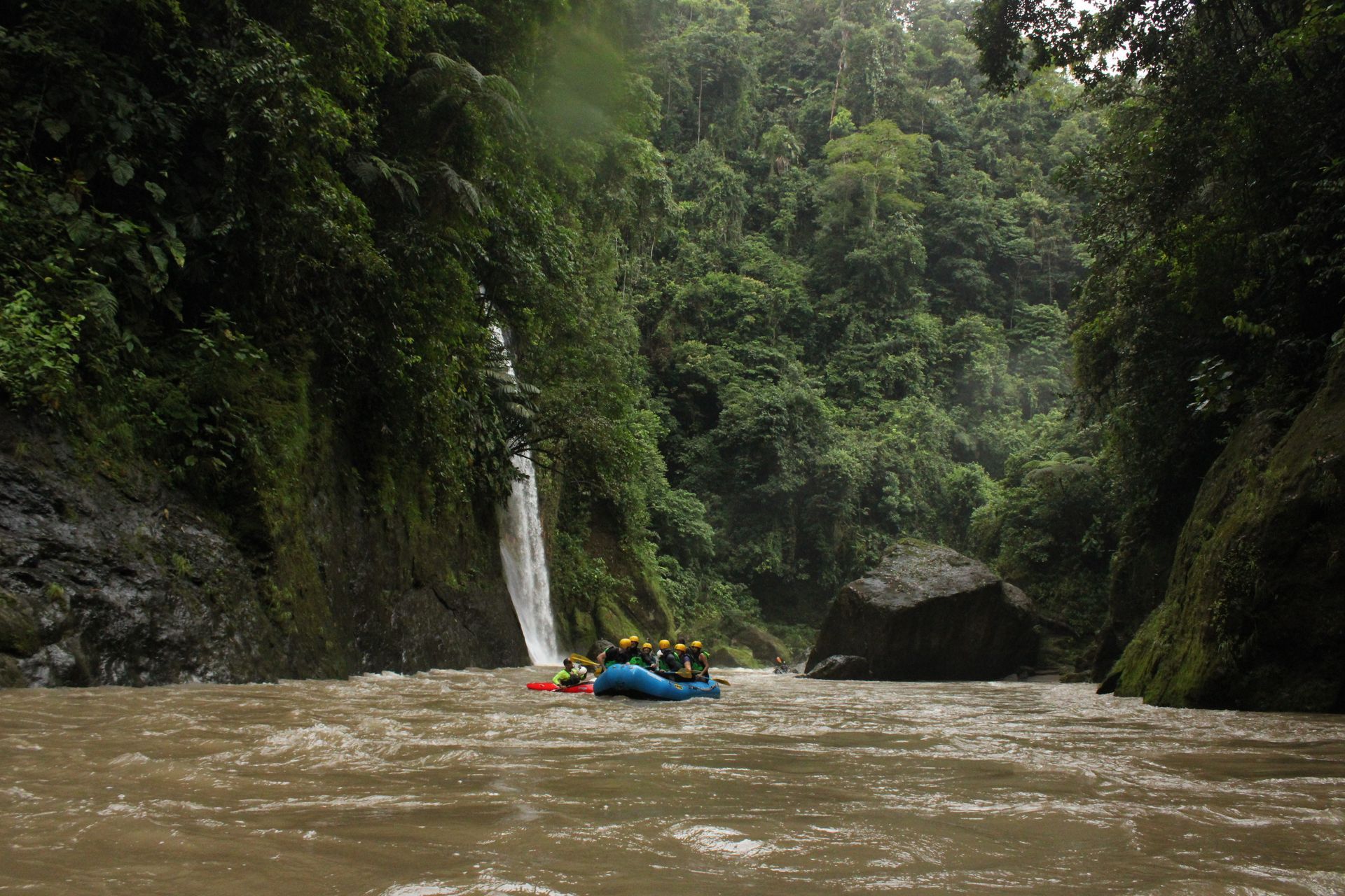 A group of people are rafting down a river near a waterfall.
