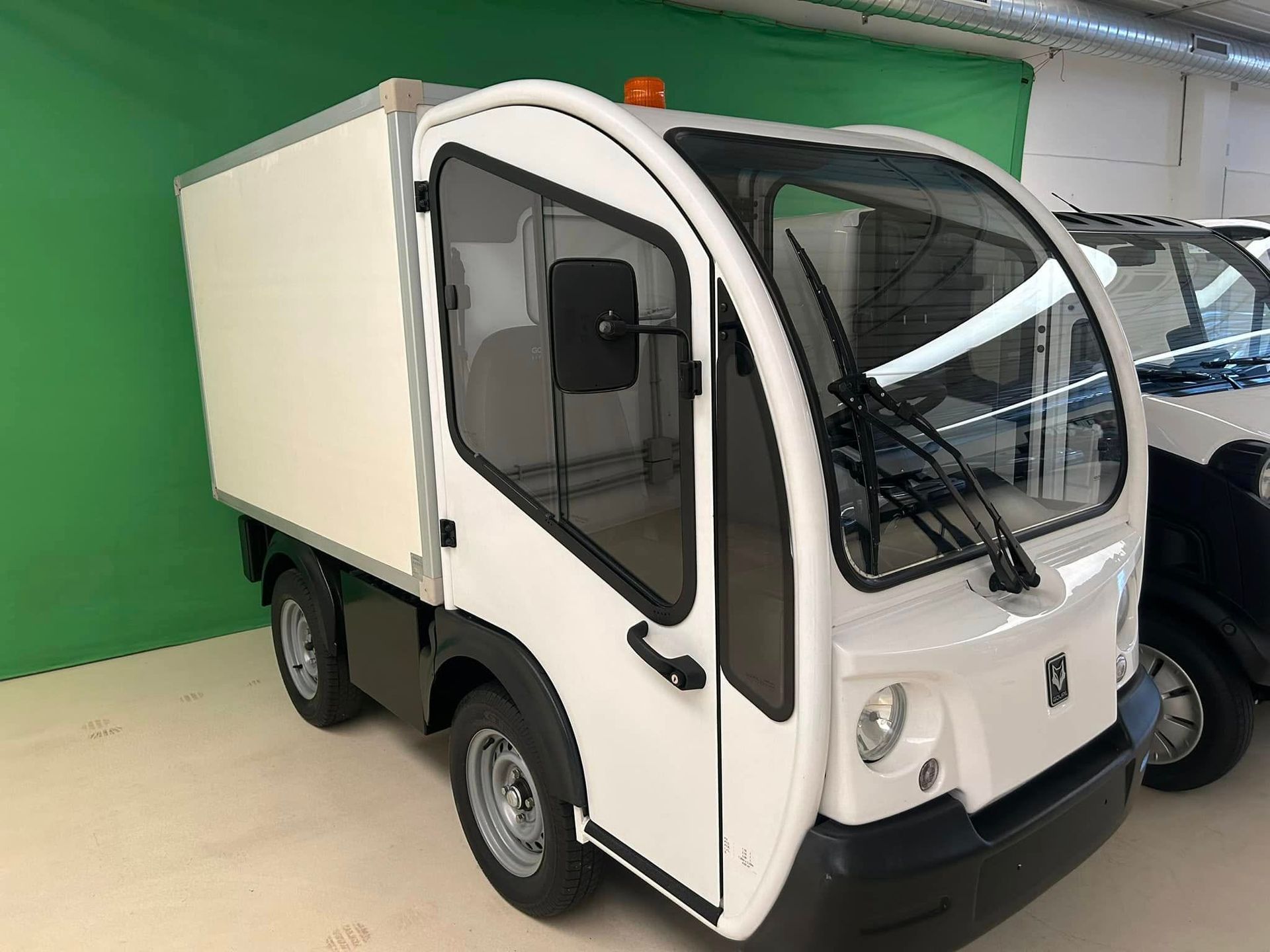 Un camion bianco è parcheggiato davanti a uno schermo verde.