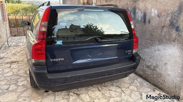 Una Volvo V70 Station Wagon blu è parcheggiata davanti a un muro di pietra.