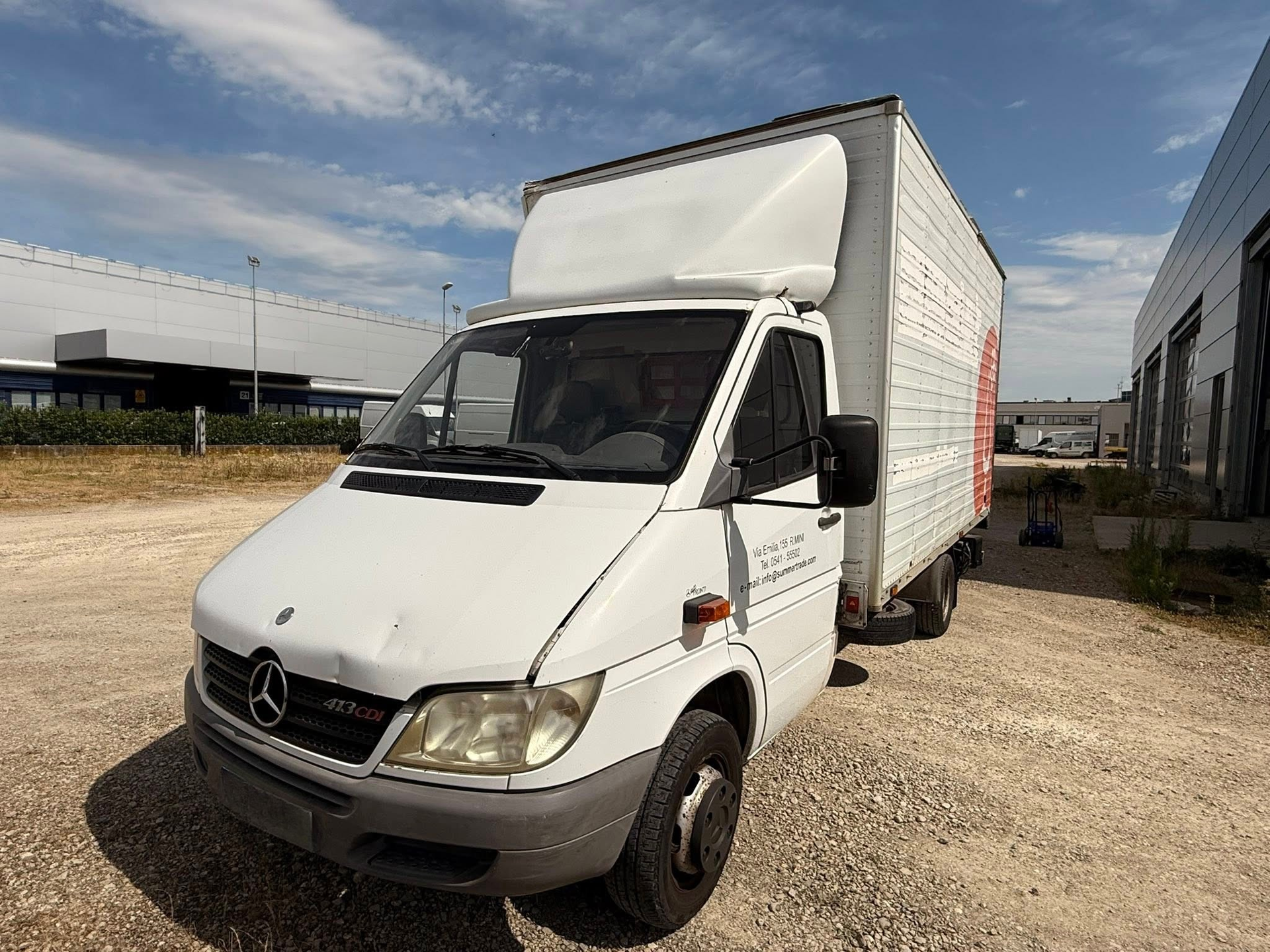 Un furgone Mercedes bianco è parcheggiato in un piazzale ghiaioso