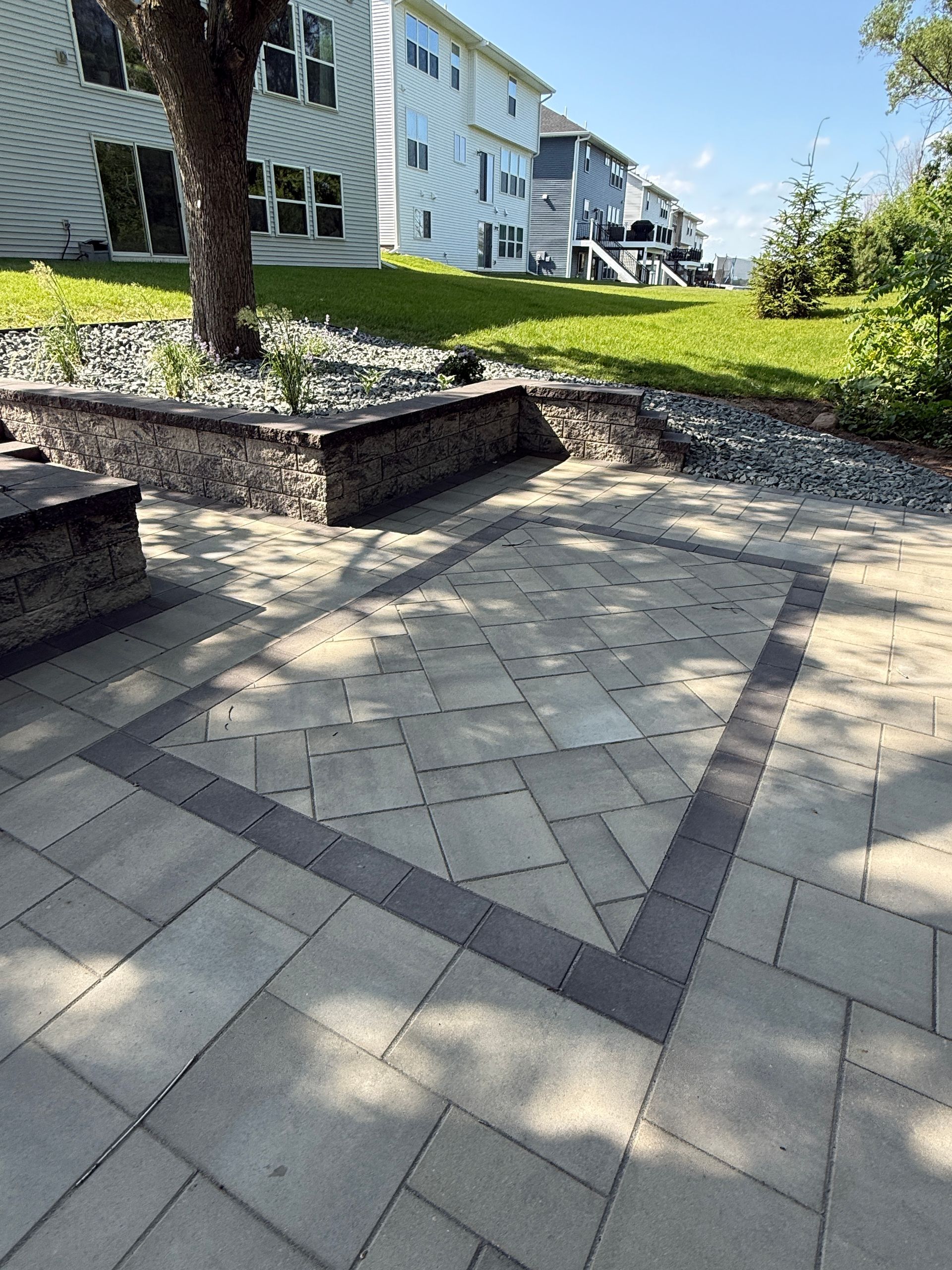 Stone patio with decorative brick border and retaining wall, leading to a grassy yard.