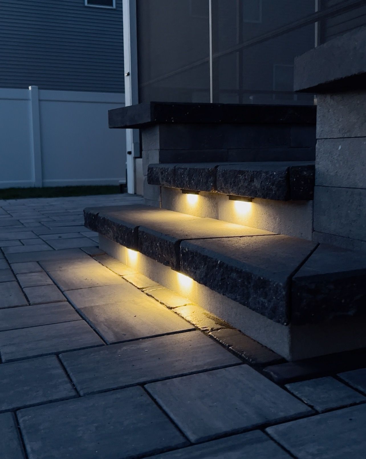 Stone steps with built-in lights illuminated, set on a stone patio at dusk.