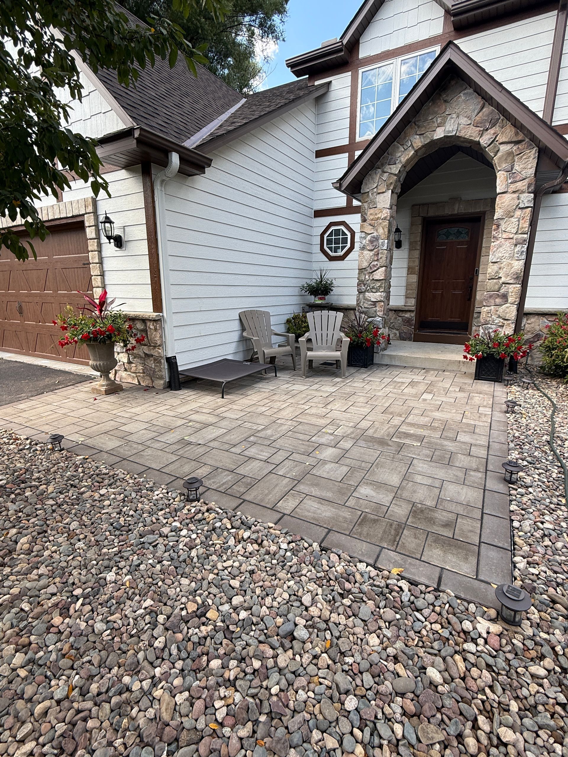 Exterior of a house with a stone archway, front door, and patio with gravel and pavers.