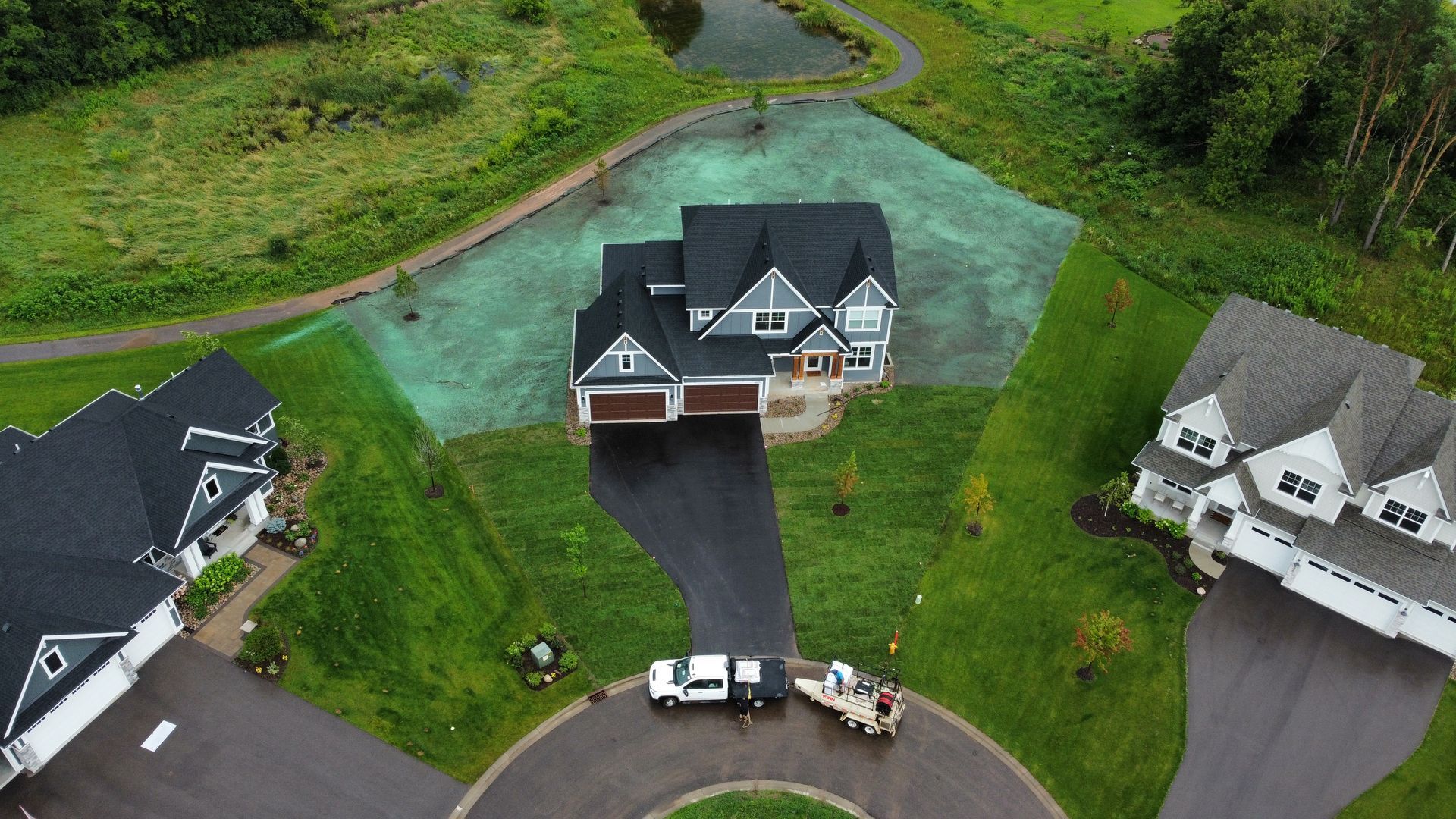 Aerial view of a house with hydroseeding lawn, workers, and other homes in a green neighborhood.