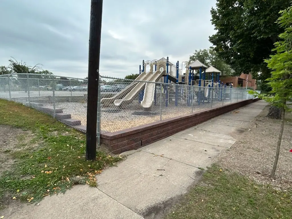 Playground with slides and climbing structures behind a chain-link fence on a cloudy day.