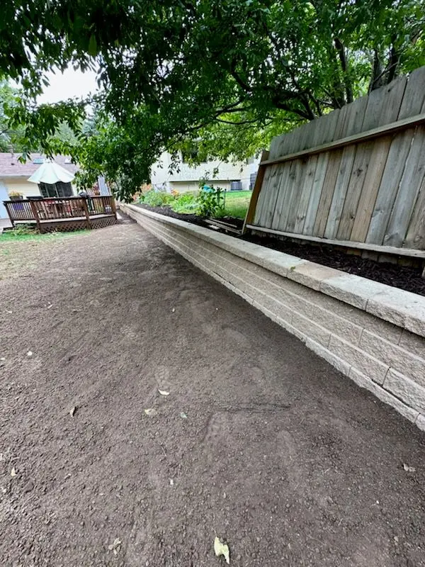 A dirt pathway alongside a raised garden bed with a wooden fence in a yard.