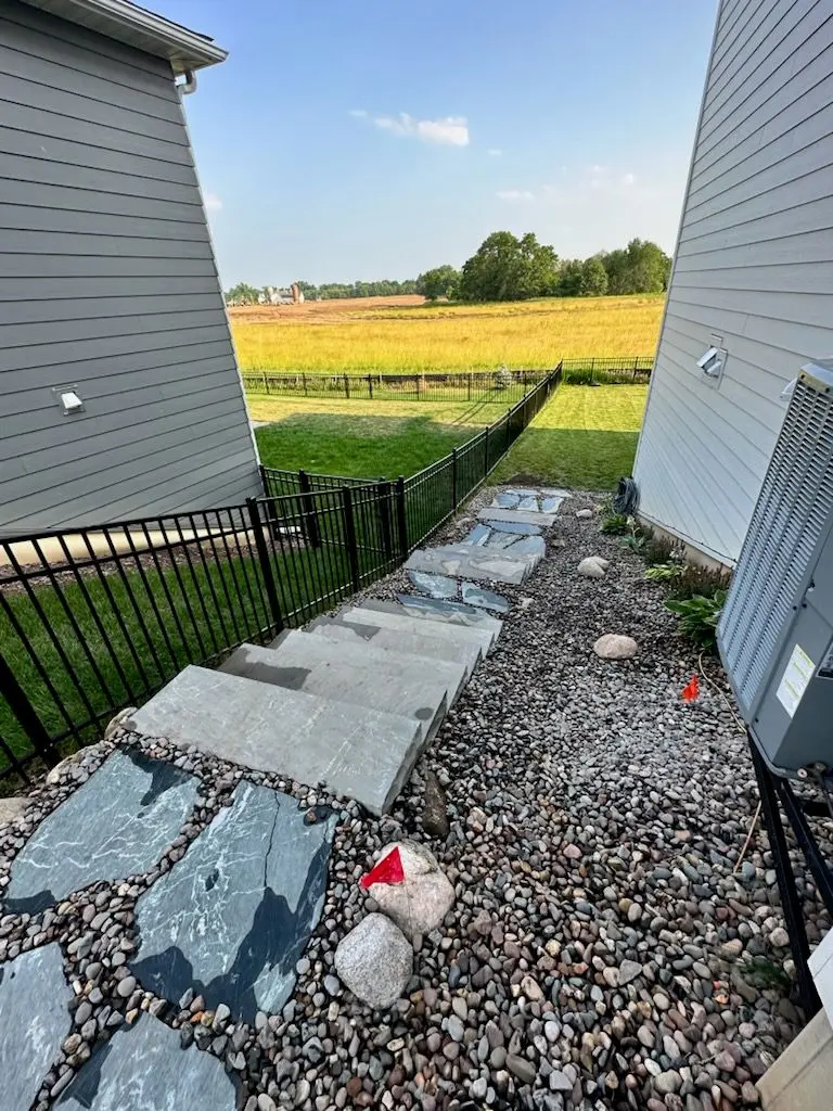 Backyard with concrete steps, stone path, gravel, black fence, and view of a field.