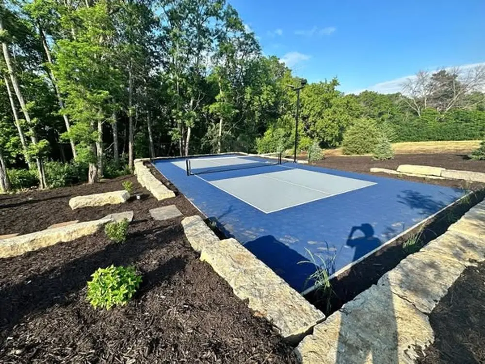 Blue and gray sports court surrounded by landscaping and trees.