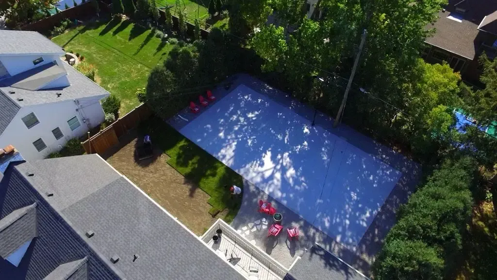 Aerial view of a rectangular pool with red chairs, surrounded by grass, trees, and houses.