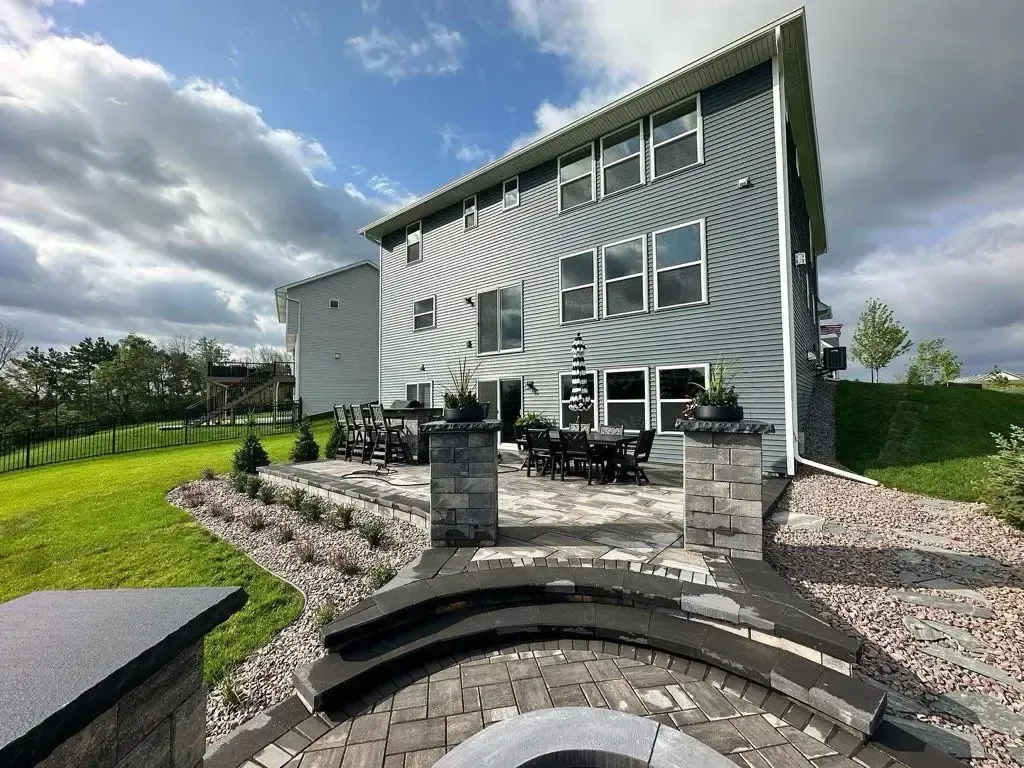 Backyard patio with gray house, landscaped yard, stone steps, and cloudy sky.