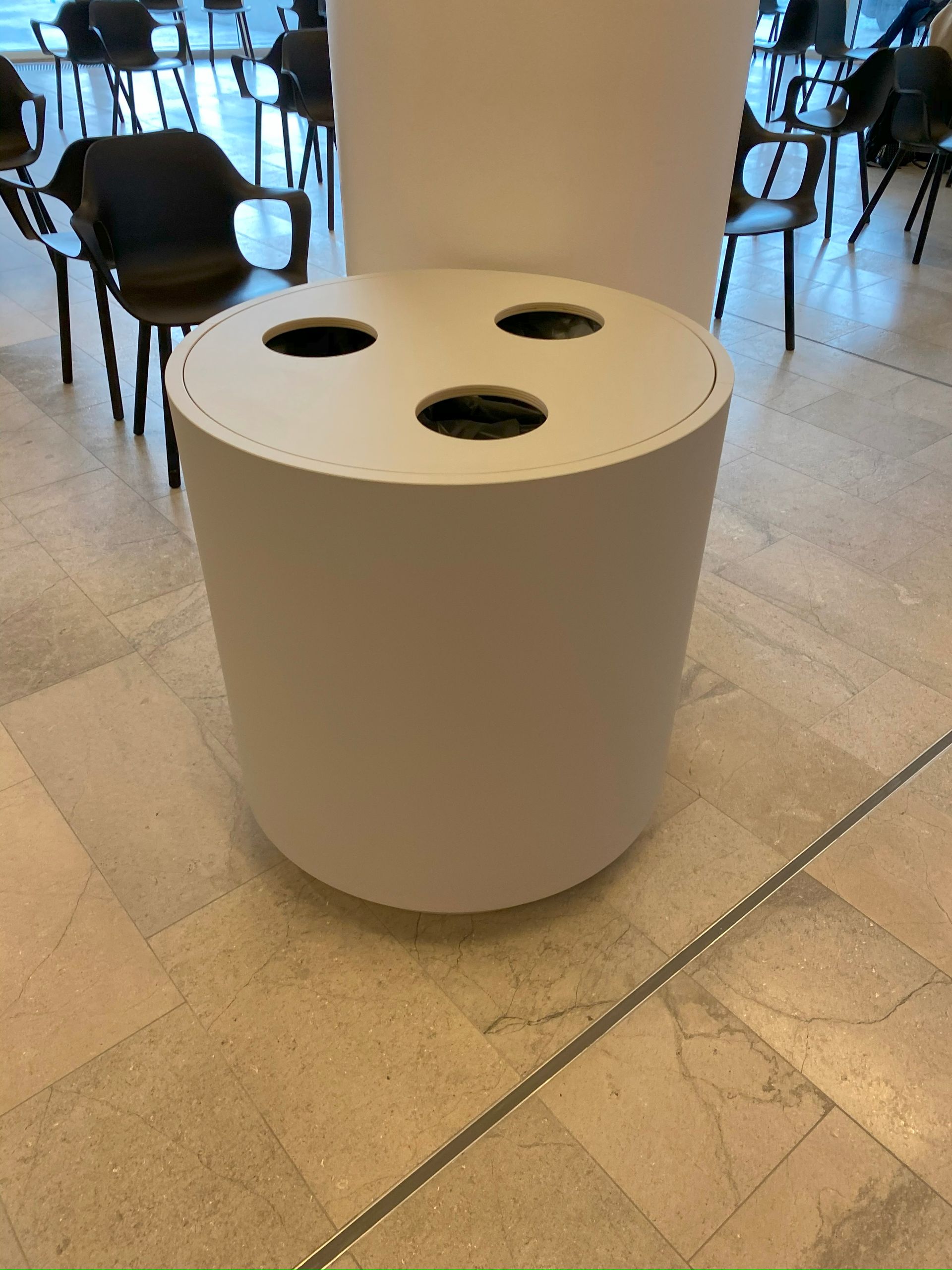 En hvid skraldespand med tre huller i står på et klinkegulv.