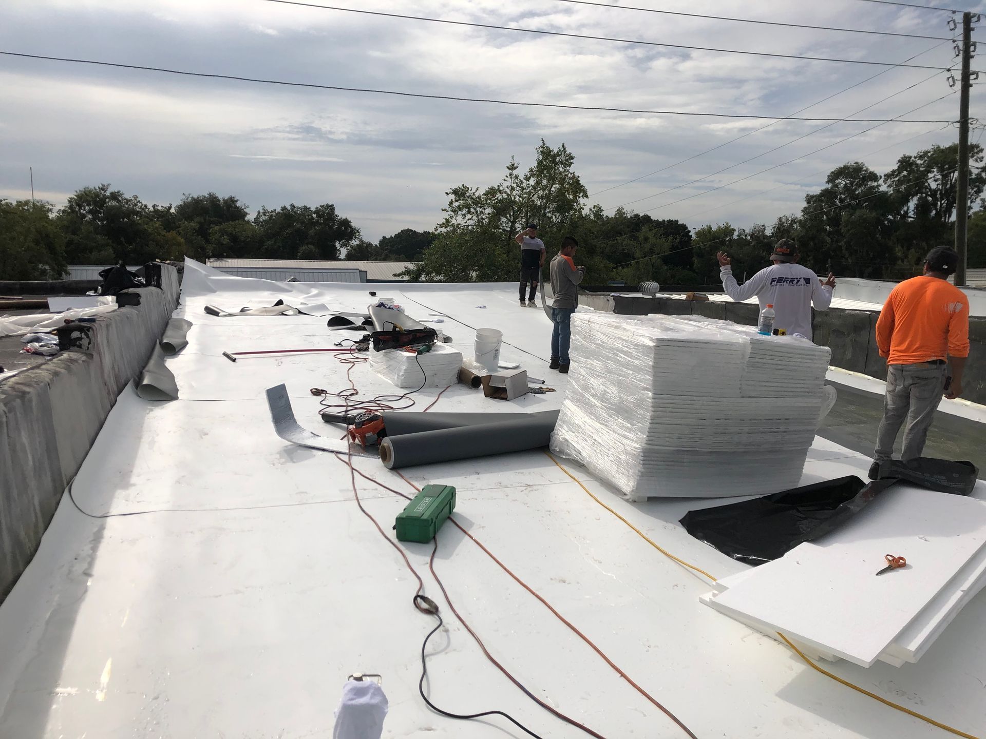 The upper level of a commercial building showing the flat roof. There are four men from Worthmann Roofing working on the flat roof with materials laid around the roof.