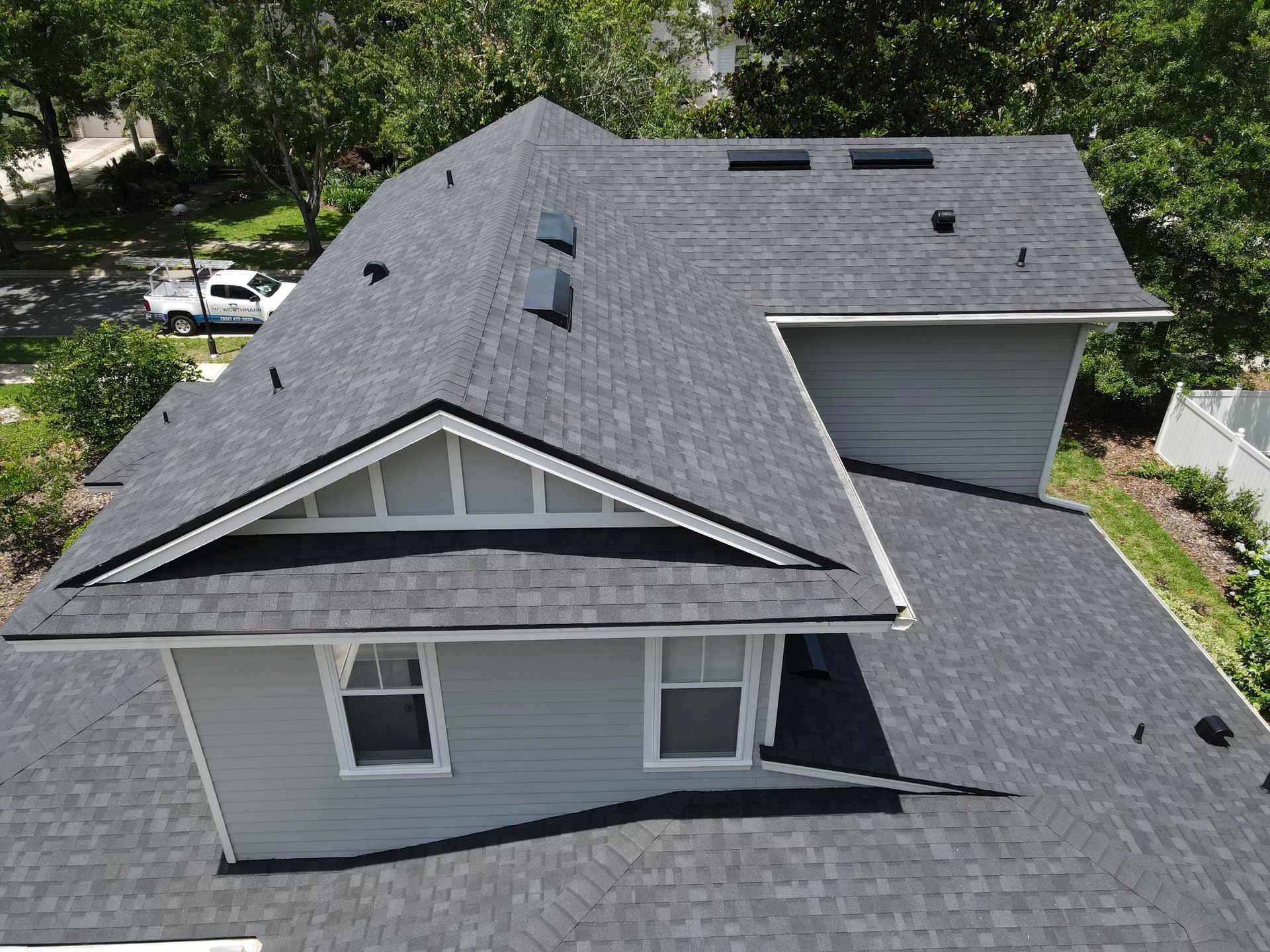 An aerial view of a residential home showing a new and clean roof made of dark-colored shingles.