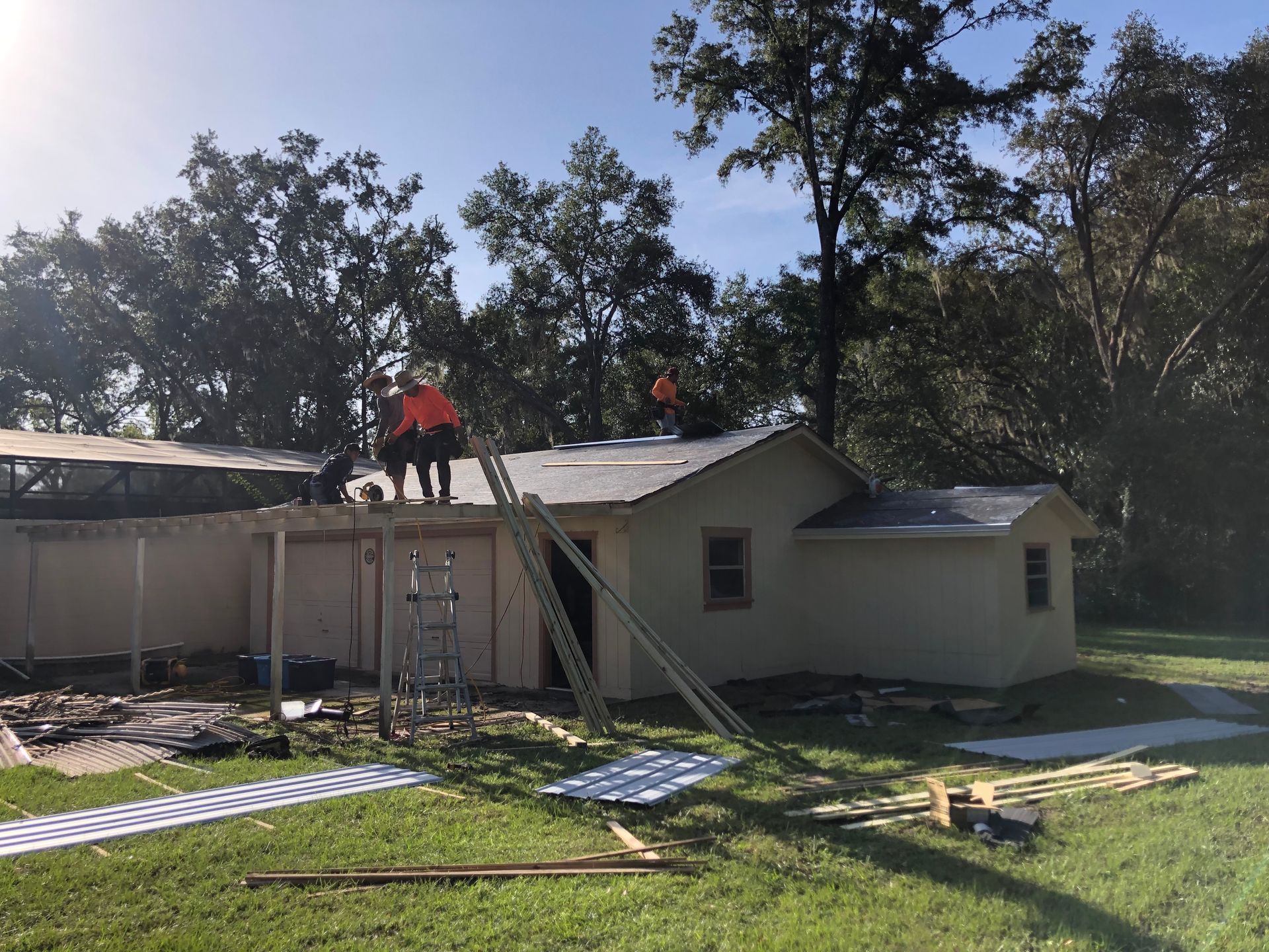 A beige-colored house having its roof repairing by four men from Worthmann Roofing. They are fixing  the base of  the roof material. There are materials scattered around the floor. At the background there is a forest.