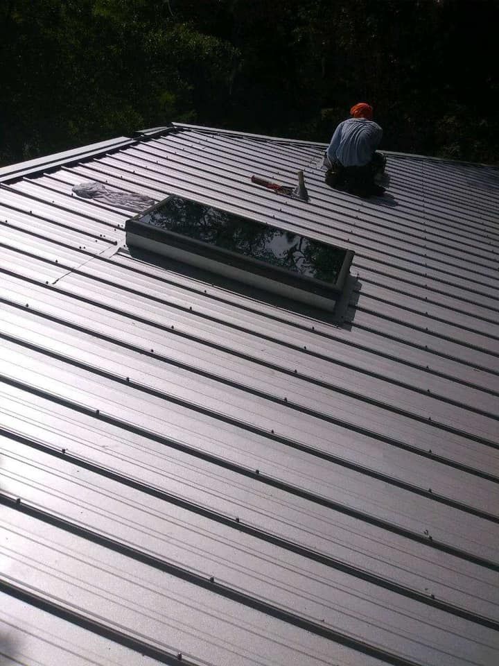 A man is sitting on top of a metal roof with a skylight