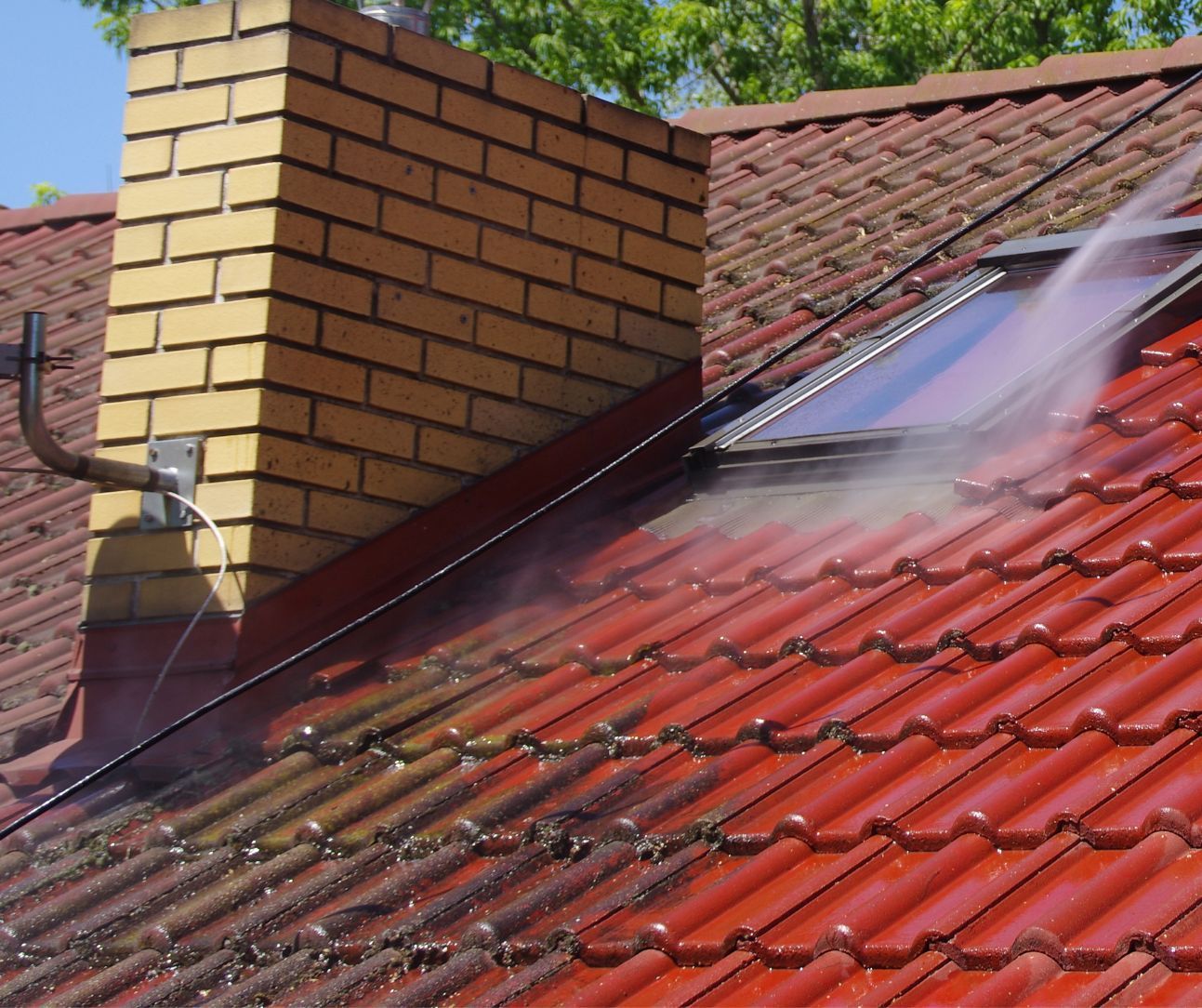 A red-tiled roof being cleaned and washed by experts, removing dirt.