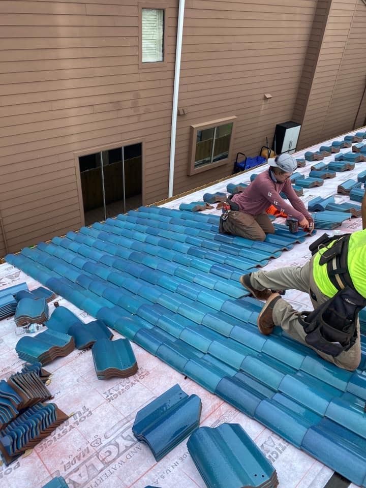 Two men are working on a roof with blue tiles.