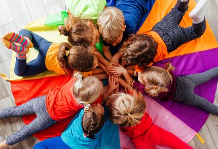 A group of children are laying in a circle on a colorful parachute.