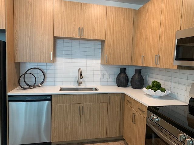 A modern kitchen with light wood cabinets, white tiled backsplash, white countertops, and stainless steel appliances.