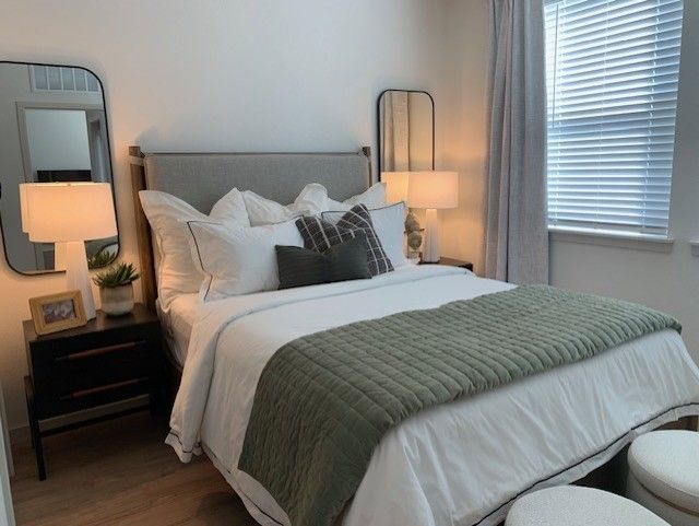 A modern bedroom featuring a bed with white bedding, an olive green throw blanket, two bedside lamps, and wall mirrors.